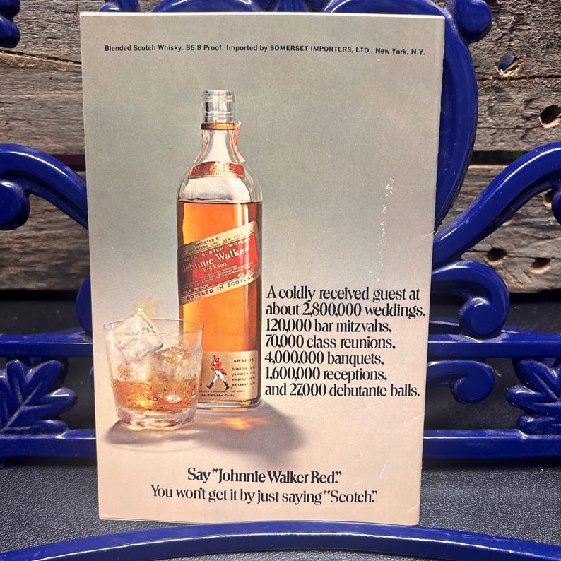 May include: An advertisement for Johnnie Walker Red blended scotch whisky. The image features a bottle of whisky with a red label, a glass of whisky with ice, and text that reads "Say 'Johnnie Walker Red.' You won't get it by just saying 'Scotch.'"