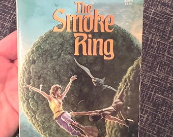 May include: A paperback book titled "The Smoke Ring" by Larry Niven. The cover art features two figures in flight over a green, spherical planet, with a flying creature. The book has a blue and orange color scheme.