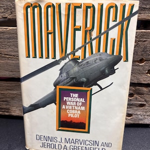 May include: A vintage book titled "Maverick" with a helicopter illustration. The cover features the text "The Personal War of a Vietnam Cobra Pilot" and the authors' names. The book has a worn appearance.