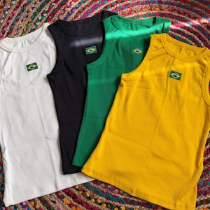 May include: Four sleeveless vests in white, black, green, and yellow. Each vest features a small Brazilian flag patch. The vests are displayed on a colourful, patterned surface.