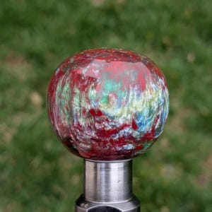 May include: A red, green, and blue swirl resin gear shift knob with a silver metal base.