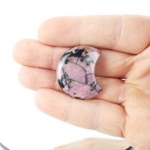 May include: A pink and black crescent-shaped cabochon of rhodochrosite gemstone.