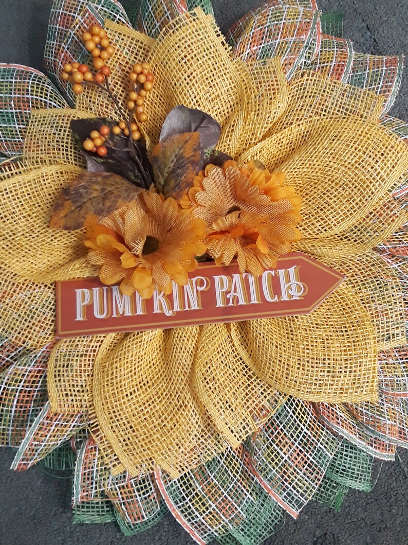 May include: A yellow and green burlap wreath with orange flowers and a sign that says "Pumpkin Patch".