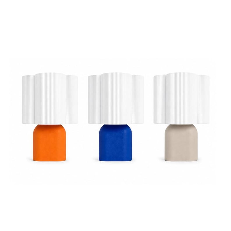 May include: Three table lamps featuring white, vertically ribbed, cylindrical shades. Each lamp has a solid, rounded, arch-shaped base in a distinct color: one is bright orange, one is deep blue, and one is a neutral beige tone.