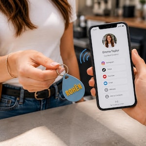 Pode incluir: Um porta-chaves NFC azul em forma de gota com o texto amarelo ROHËN preso a um anel prateado. Um smartphone exibe um perfil digital para Emma Taylor, Content Creator, com ícones para Instagram, TikTok, YouTube, Email, Website e Add to Contacts.