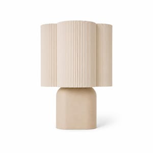 May include: A table lamp featuring a beige, vertically ribbed, scalloped cylindrical shade atop a smooth, solid, rounded rectangular base. The lamp has a uniform light tan color throughout, with a distinct contrast between the textured shade and the matte base.