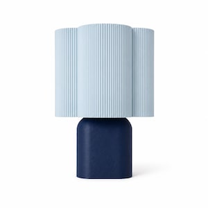 May include: A table lamp featuring a light blue, vertically ribbed, cloud-shaped shade positioned atop a solid, dark navy blue, rounded rectangular base. The lamp has a clean, two-tone design with a textured finish on the base.