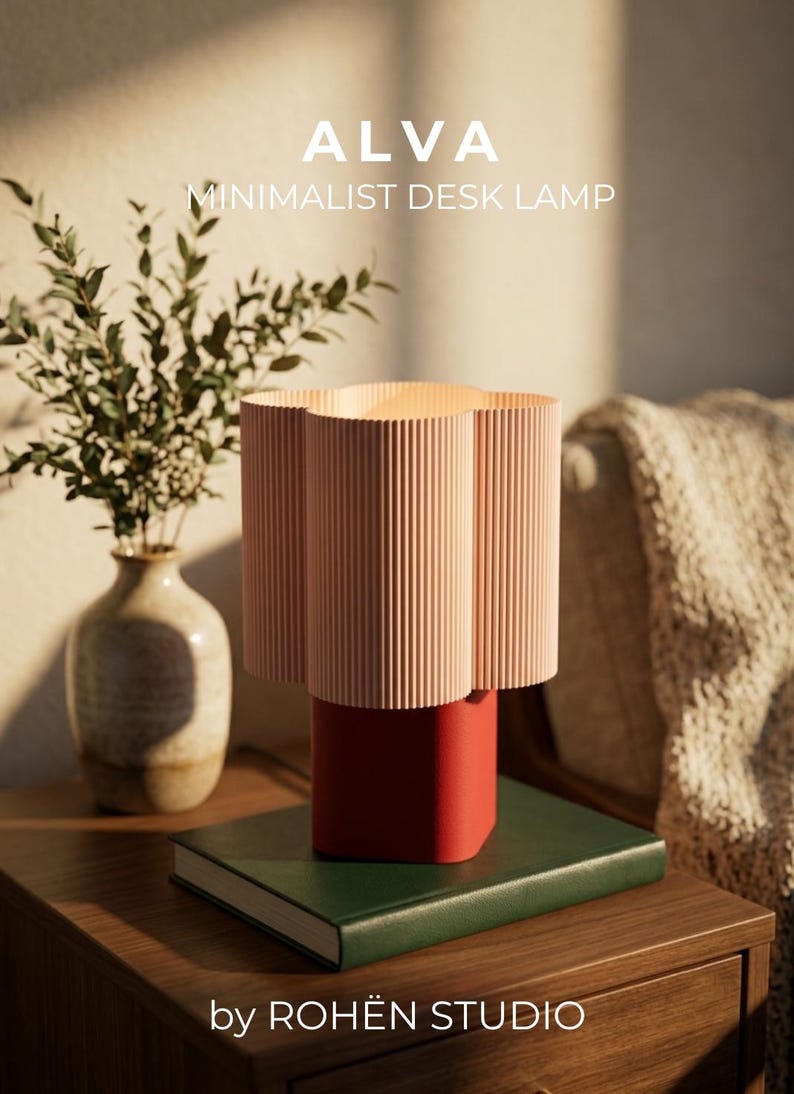 A desk lamp with a light pink, vertically ribbed, flower-shaped shade and a solid red rectangular base. The text ALVA MINIMALIST DESK LAMP by ROHËN STUDIO is visible in the upper and lower portions of the image, respectively.