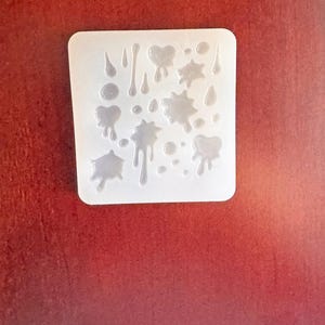 May include: A clear, rectangular silicone mold with various shapes, including hearts, stars, and droplets. The mold is designed for crafting resin art and jewelry. The shapes are arranged across the surface of the mold.