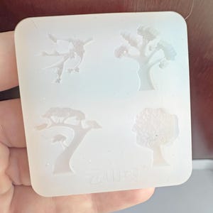 May include: A clear, square silicone mold featuring four tree designs. The designs include a stylized figure, a tree with a full canopy, a tree with a small mushroom, and a tree with a rounded crown. The text "云山阁" is printed at the bottom.