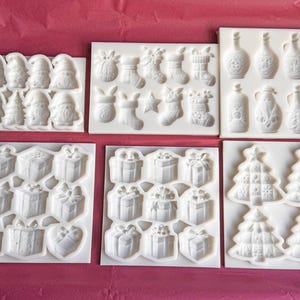Puede incluir: Un conjunto de moldes de silicona blancos con diseños navideños. Los moldes incluyen figuras de Papá Noel, cajas de regalo, calcetines navideños, adornos, botellas y árboles de Navidad. Ideales para crear decoraciones festivas.