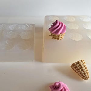 May include: Two silicone moulds for crafting, one with petal shapes and the other with multiple ice cream cone impressions. A finished miniature ice cream cone with pink swirl and a waffle cone are also present. The moulds are white and the ice cream is pink and brown.