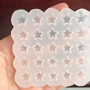 May include: A clear silicone mould with a scalloped edge, featuring a grid of star-shaped cavities. The mould is held in a hand, showcasing its translucent quality and the detailed star impressions.