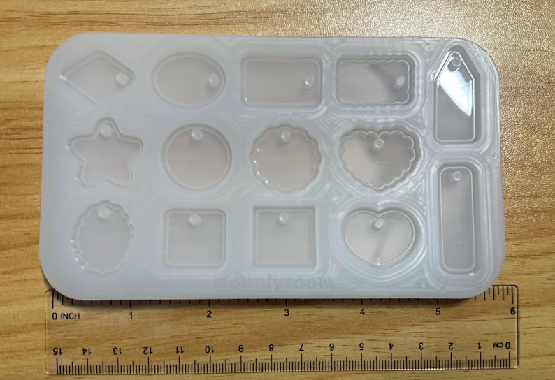 May include: A clear, rectangular silicone mold with various shapes, including a star, heart, and tag designs. The mold is on a wooden surface, with a ruler showing measurements in inches.