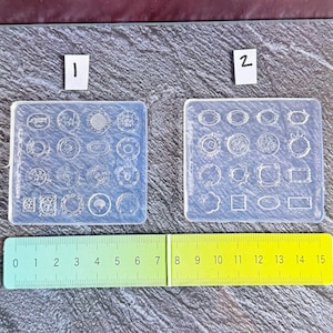 May include: Two clear silicone molds with various circular and rectangular shapes for crafting. A ruler shows measurements up to 6 inches. The molds are ideal for resin jewelry or decorative elements.