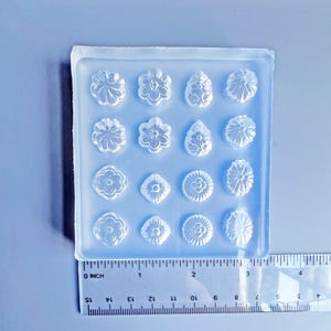 May include: A clear, rectangular silicone mold with various floral designs. The mold features detailed flower, leaf, and geometric shapes, with a ruler along the bottom for size reference. The mold is approximately 4 inches wide.