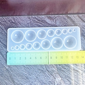 May include: A clear silicone mold with various sized circular cavities. A ruler is placed next to the mold, showing measurements up to 14 inches. The mold is designed for crafting or resin projects, offering a range of circle sizes.