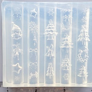 May include: A clear silicone mould featuring festive Christmas designs. The mould includes embossed images of a gingerbread man, Santa Claus, stars, snowflakes, bells, bows, Christmas trees, and wreaths. Ideal for crafting decorative items.