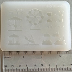 Könnte beinhalten: Eine rechteckige, cremefarbene Silikonform mit verschiedenen Designs zum Thema Vergnügungspark. Die Designs umfassen ein Riesenrad, ein Karussell, Autoscooter und eine Schaukel. Der Text "Cold Bubble" ist sichtbar. Ein Lineal liegt darunter. Die Form ist ca. 7,6 cm breit.