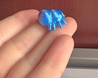 May include: A small, blue, 3D-printed object resembling a sea creature, held in a hand. The object has a rounded body and multiple appendages. The color is a vibrant, solid blue.
