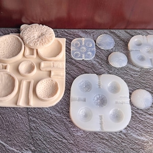 May include: A collection of silicone molds and a beige plaster mold. The silicone molds are clear and feature various circular and spherical shapes. The plaster mold has a variety of bowl-like shapes and a mushroom-shaped top.
