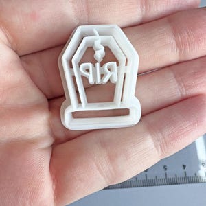 Op de afbeelding: Een witte plastic koekjesvorm in de vorm van een grafsteen met de letters "RIP". De vorm heeft een rechthoekige basis en een gestileerde bovenkant met een kleine lus. Ideaal voor Halloween-bakken.