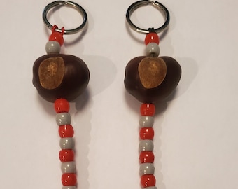 May include: Two keychains with red and gray beads and brown chestnut shells. The keychains are attached to silver key rings.