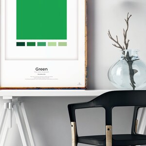 May include: A framed poster with a large green square and a smaller row of green squares below it. The poster has the word "Green" and the text "The color of growth" printed on it. The poster is on a white table with a black chair and a clear glass vase with a branch.