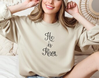 May include: A beige sweatshirt with the text "He is Risen" in black cursive lettering.
