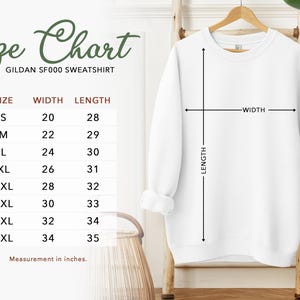 a size chart for a GILAN SF500 sweatshirt, with measurements for different sizes ranging from S to M. The chart is accompanied by a wooden hanger and a plant, creating a casual and relaxed setting.