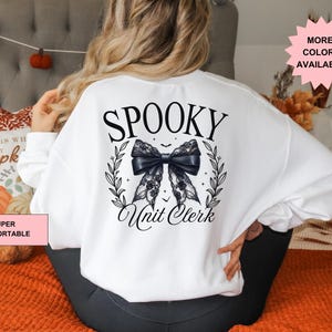 May include: White sweatshirt with the text "Spooky Unit Clerk" in black lettering. A black lace bow with a white outline and bats is above the text.