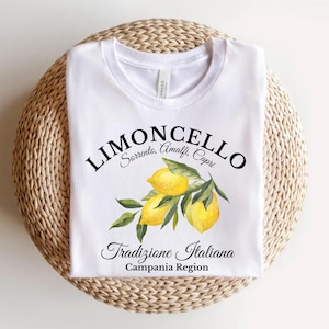 Pu&ograve; includere: Una t-shirt bianca con una grafica raffigurante tre limoni gialli con foglie verdi. Il testo LIMONCELLO, Sorrento, Amalfi, Capri, Tradizione Italiana e Campania Region &egrave; stampato in nero al centro della parte anteriore del capo.