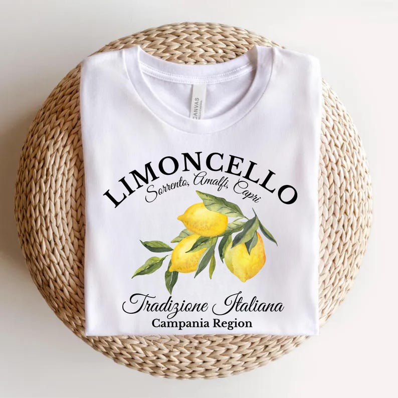 Pu&ograve; includere: Una t-shirt bianca con una grafica raffigurante tre limoni gialli con foglie verdi. Il testo LIMONCELLO, Sorrento, Amalfi, Capri, Tradizione Italiana e Campania Region &egrave; stampato in nero al centro della parte anteriore del capo.