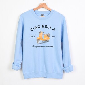 K&ouml;nnte beinhalten: Hellblauer Pullover mit einem gelben Roller-Motiv und dem Text "Ciao Bella Since 1861 La migliore estate di sempre".
