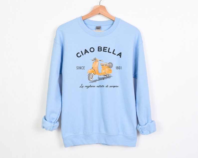 K&ouml;nnte beinhalten: Hellblauer Pullover mit einem gelben Roller-Motiv und dem Text "Ciao Bella Since 1861 La migliore estate di sempre".