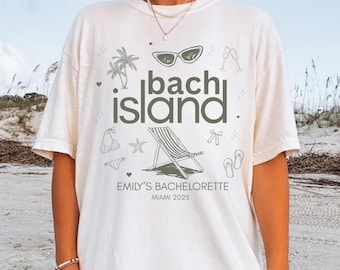 May include: Off-white t-shirt with the text "Bach Island" in green, along with beach-themed illustrations. The shirt also includes the text "Emily's Bachelorette Miami 2025". The design features sunglasses, palm trees, a beach chair, and other summer elements.
