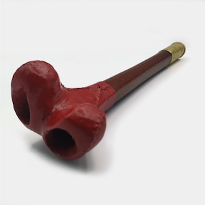 May include: A red wooden smoking pipe with a brass mouthpiece. The pipe has a unique, curved design with two holes.