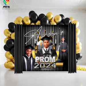 May include: Black and gold prom backdrop with the text "Aaron's Prom 2024". Two people in graduation robes are standing in front of the backdrop.