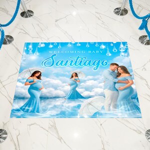 May include: A blue welcome baby sign with the name "Santiago" in cursive. The sign features illustrations of a pregnant person in a blue dress, a couple, and umbrellas. The background is a sky with clouds.