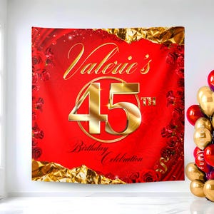 May include: A red birthday banner with gold text that reads "Valerie's 45th Birthday Celebration." The banner has a gold frame and is decorated with red roses. A cluster of gold and red balloons is visible on the right.