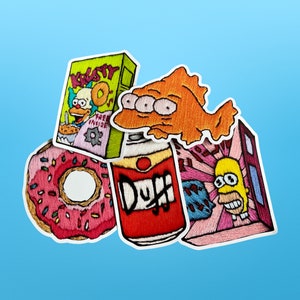 May include: Five embroidered iron-on patches featuring popular cartoon characters and food items. The patches include a box of Krusty-O's cereal, a can of Duff beer, a pink donut, a three-eyed fish, and a cartoon character with yellow skin and a blue shirt.