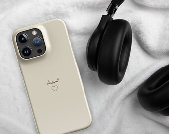 May include: A beige smartphone case with a triple-lens camera is next to black over-ear headphones. The phone case has Arabic text and a heart symbol. The items are on a white, textured surface.