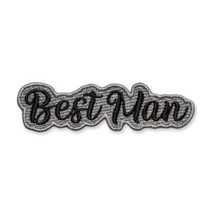 May include: Embroidered patch with the words "Best Man" in black script lettering. The text is outlined with a gray border. The patch has a gray fabric background and is designed to be sewn or ironed onto clothing or accessories.