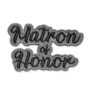 May include: Embroidered patch with the words "Matron of Honor" in black script lettering. The text is on a gray denim-like background with a black border. The patch is designed to be sewn or ironed onto fabric.