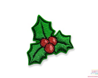 May include: A green holly leaf with three red berries. The holly leaf is embroidered with a green thread and the berries are embroidered with a red thread.
