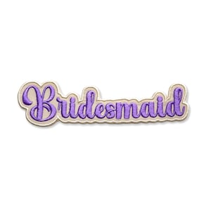 May include: A purple embroidered patch with the word "Bridesmaid" in a cursive font. The text is outlined in a light tan color, and the patch has a scalloped edge. The background is white.