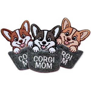 May include: Three embroidered patches featuring cartoon Corgi dogs peeking out of dark gray pockets. Each pocket is stitched with the white text CORGI MOM. The dogs are brown, black, and tan with white markings, large eyes, and happy expressions.