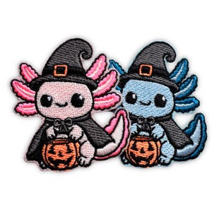 May include: Two embroidered patches featuring cartoon axolotls wearing black witch hats and capes. One axolotl is light pink with bright pink gills, and the other is light blue with dark blue gills. Both hold orange jack-o'-lantern candy buckets.