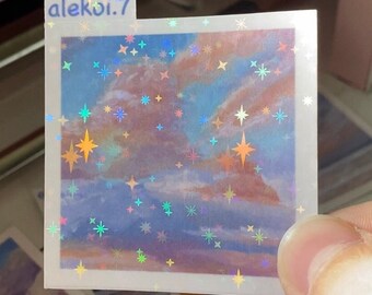 May include: A holographic sticker with a blue and pink sky with clouds and stars. The sticker has a white border and the text "alekoi.7" in the top left corner.