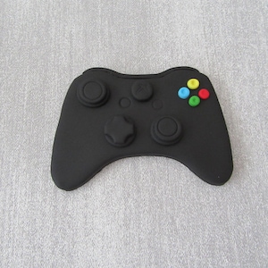 May include: A black plastic video game controller with four coloured buttons. The buttons are red, yellow, blue and green.